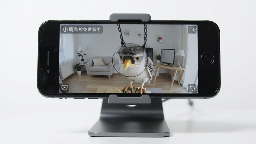 小鹰监控免费看家应用界面展示,主体为一部旧手机被改造成监控摄像头,布局为手机居中放置于桌面支架上,排版简洁,风格为现代科技感,细节包括手机屏幕上显示实时监控画面,画质清晰,干净,无多余元素